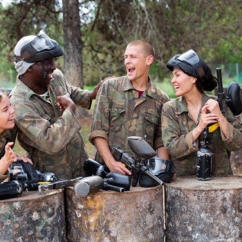 Five people smiling wearing paintball gear holding paintball guns